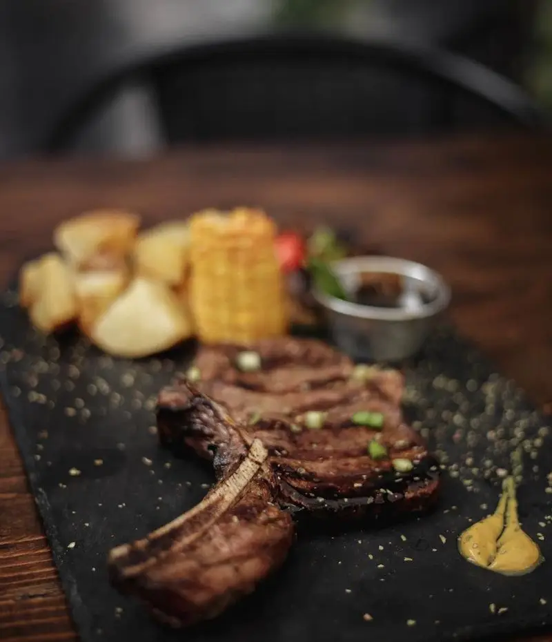 استیک دنده لذیذ کافه رد با سیب زمینی تنوری، ذرت و سس مخصوص. بهترین غذای منوی کافه رد برای تجربه یک شام یا ناهار عالی.