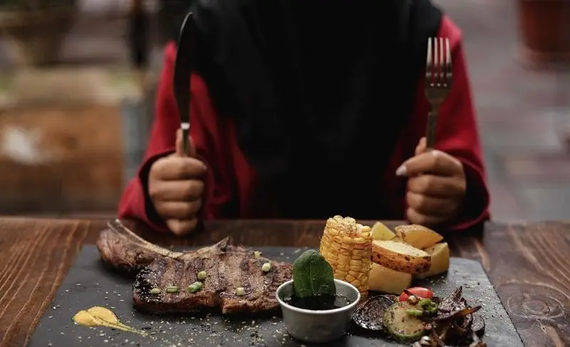 لذت چشیدن استیک گریل شده آبدار با دورچین متنوع سیب زمینی، ذرت و سبزیجات تازه در فضای دلنشین رستوران کافه رد.