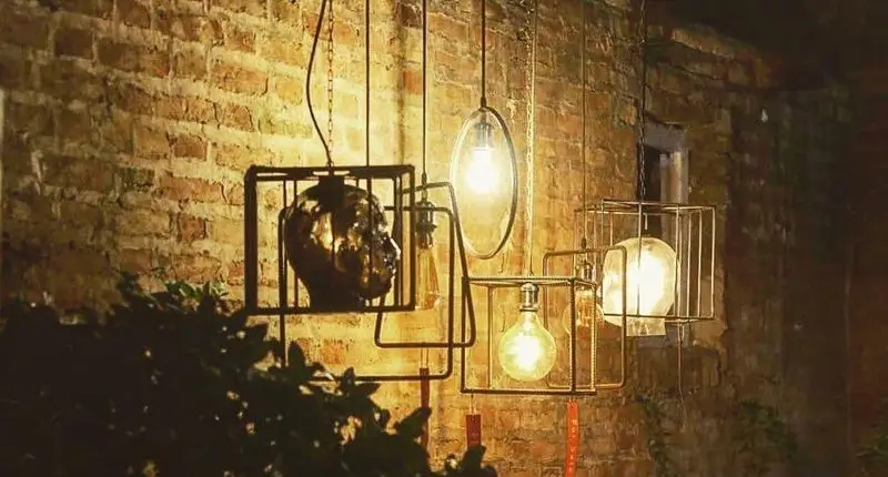 نورپردازی جذاب کافه رد با لامپ‌های آویز مدرن در قاب‌های فلزی و سر مجسمه بر روی دیوار آجری، فضایی دلنشین و خاص.