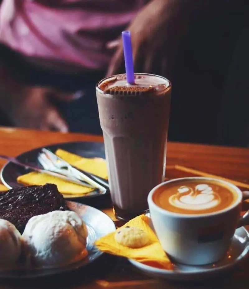 تصویری جذاب از منوی کافه رد: میلک شیک شکلاتی، قهوه لاته با طرح قو، براونی شکلاتی با بستنی و کوکی در محیطی دلنشین.