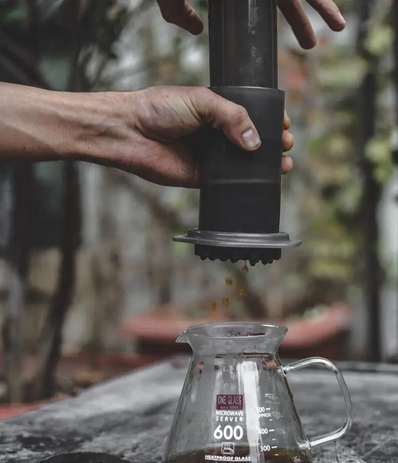 فرایند دم‌آوری قهوه با ایروپرس توسط باریستا در کافه رد. قهوه داغ و تازه در حال ریخته شدن به سرور شیشه‌ای، لذت یک فنجان عالی.