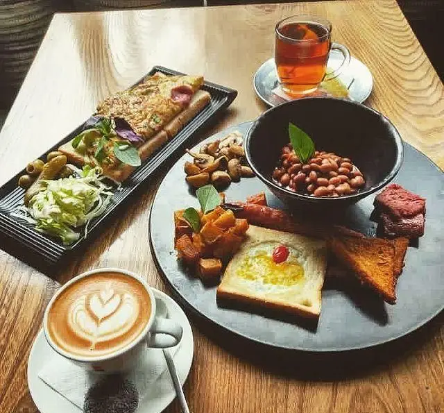 صبحانه ویژه کافه رد: میز پر از خوراکی شامل املت، لوبیا، سوسیس، نان تست، قارچ، سبزیجات تازه، لاته و چای داغ و دلپذیر.