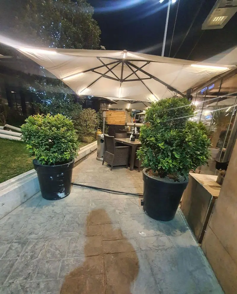 کافه رستوران لایم، فضای باز دلنشین شبانه با سایبان‌های نورانی، میز و صندلی‌های شیک و گیاهان سرسبز برای تجربه‌ای خاص.