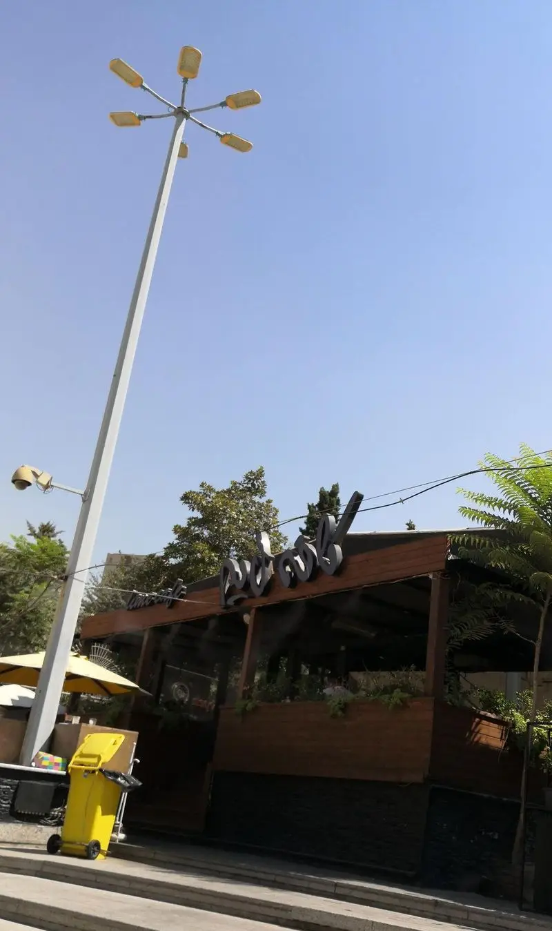 تصویر نمای بیرونی کافه رستوران لایم، تابلوی خاص کافه در روز روشن. فضای دنج بیرونی با چترها و تیر چراغ برق در حاشیه خیابان.