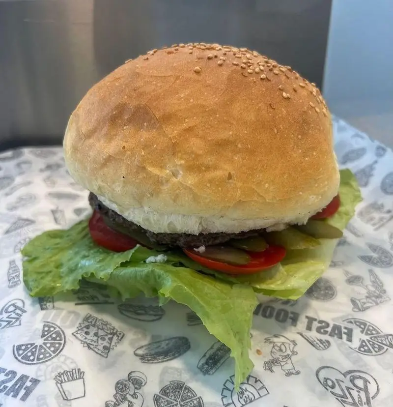 تصویری جذاب از یک همبرگر خوشمزه و پرملات با نان کنجدی، کاهو تازه، گوجه و خیارشور، ارائه شده توسط پیتزا ساندویچ هیرون فود.