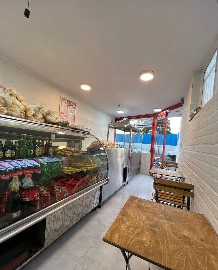 فضای داخلی جذاب فست فود پیتزا ساندویچ هیرون فود با ویترین بزرگ انواع ساندویچ، نان، نوشیدنی، سوسیس و ترشی. میز و صندلی چوبی مدرن مشتریان.