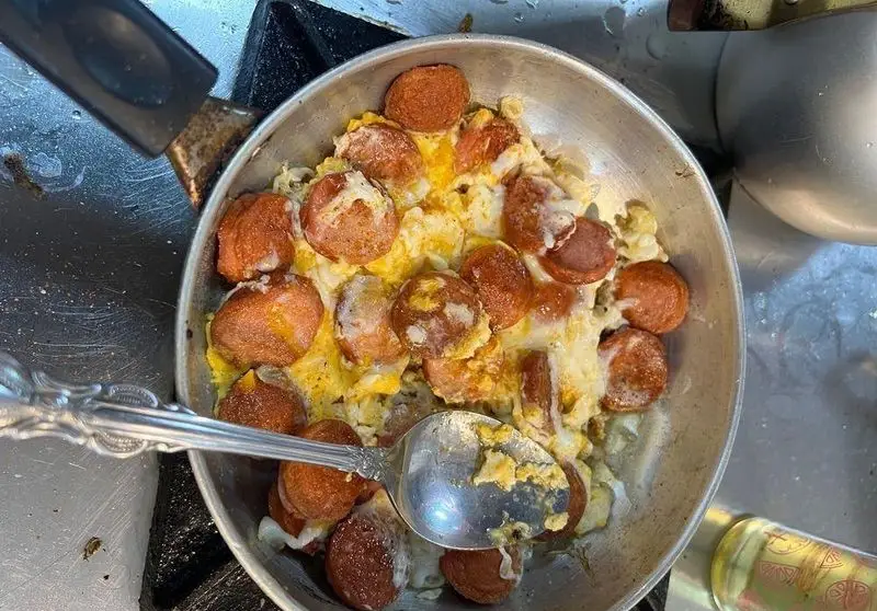 تصویری از سوسیس و تخم مرغ نیمرو داغ در تابه فلزی، یک صبحانه یا غذای سریع و لذیذ از پیتزا ساندویچ هیرون فود. آماده سرو.