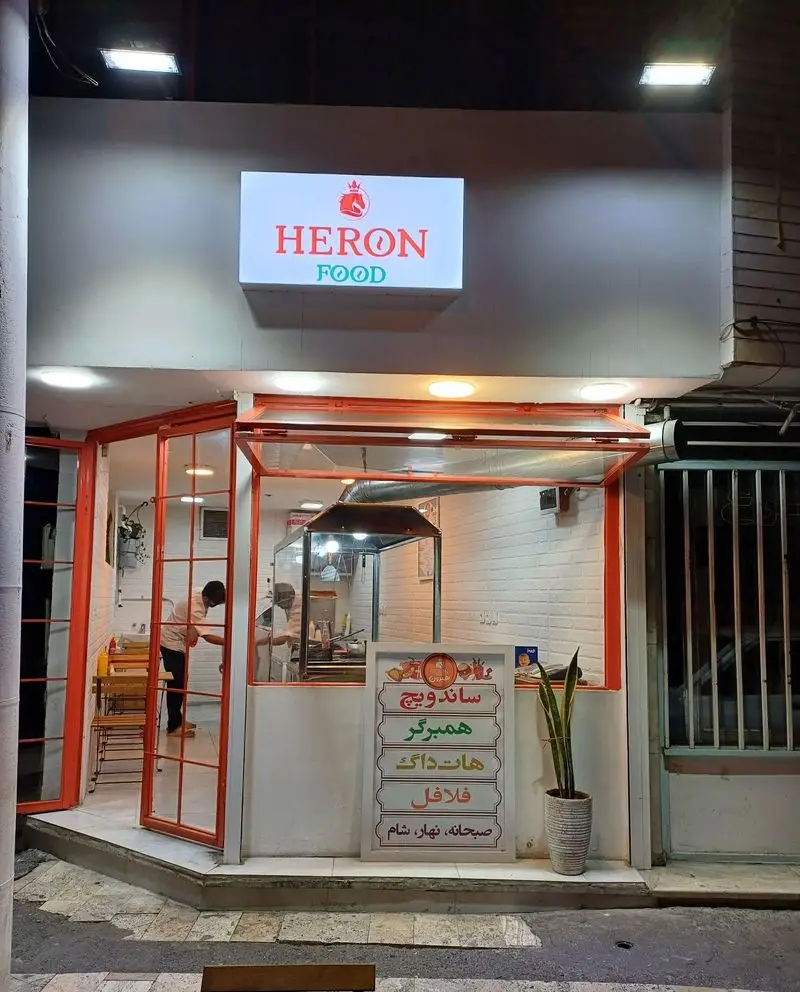 نمای شبانه فست فود و پیتزا ساندویچ هیرون فود با تابلوی روشن، منوی کامل ساندویچ، همبرگر، هات داگ، فلافل و صبحانه، نهار، شام.