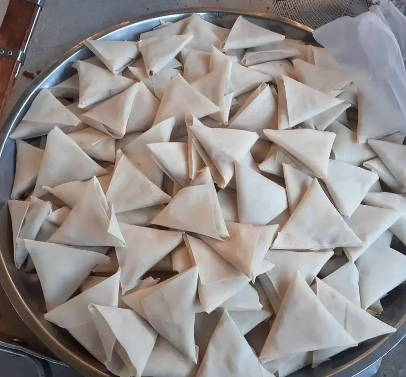 نمایی از سینی مملو از سمبوسه های مثلثی نیمه آماده و دست ساز فلافل ابوحیدر، آماده طبخ برای سفارشات شما.