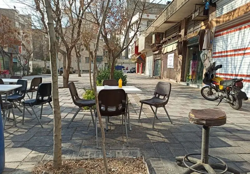 محیط بیرونی و صمیمی فلافل ابوحیدر با درختان سایه دار، میز و صندلی‌های ساده برای لذت بردن از فلافل‌های خوشمزه در فضای باز.