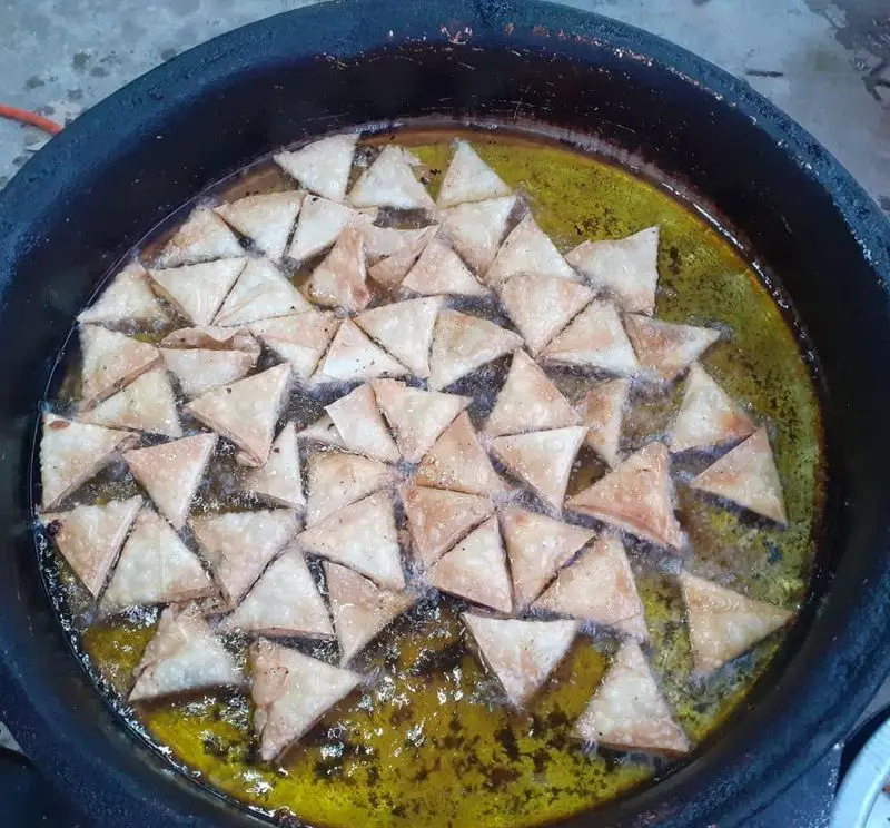 تصویری از پخت لقمه‌های مثلثی و سمبوسه‌های داغ در روغن فراوان. غذای تازه کسب و کار فلافل ابوحیدر آماده سرو است.