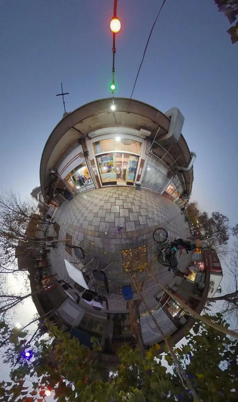 نمای بیرونی فلافل ابوحیدر در یک عصر دل‌انگیز با نورپردازی شهری، درختان، سنگفرش و صندلی‌های فضای باز، محیطی گرم.