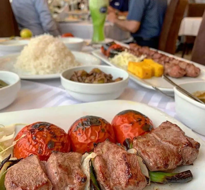 تصویری زیبا از میز پر از غذاهای لذیذ ایرانی شامل کباب کوبیده و برگ به همراه برنج و گوجه کبابی در رستوران نایب ابان.