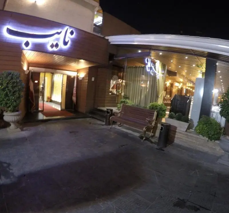 نمای بیرونی شیک و روشن رستوران نایب ابان در شب با تابلوی درخشان، ورودی مجلل و نیمکت‌های راحت برای مشتریان.