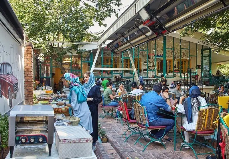 کافه شمرون: تجربه صبحانه یا ناهار در فضای باز و دلنشین کافه. مشتریان مشغول سرو غذا از بوفه رنگارنگ.