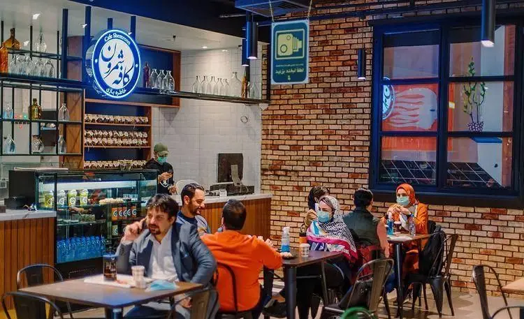 تصویری از فضای داخلی کافه شمرون با دکوراسیون مدرن آجری و مشتریانی در حال لذت بردن از نوشیدنی‌ها، مناسب پاتوق‌های دوستانه.