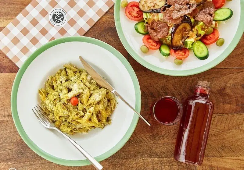 نمایی دلنشین از منوی کافه شمرون شامل پاستا پنه پستو با پنیر پارمزان، سالاد گوشت و بادمجان با چاشنی خاص، و نوشیدنی خنک در محیط دنج کافه.