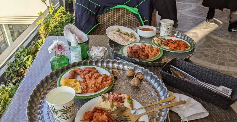 صبحانه مفصل و متنوع کافه شمرون در فضای دلنشین تراس، شامل سوسیس، تخم مرغ، زیتون، پنیر و گردو. لذت یک وعده غذایی لذیذ در کافه.