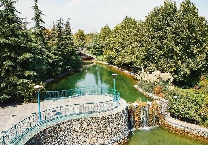 پارکی سرسبز با برکه آرام، آبشاری دلنشین، مسیر پیاده‌روی و درختان بلند، محیطی دنج و زیبا از کافه شمرون برای لذت بردن.