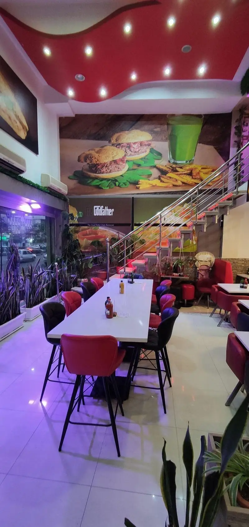 فست فود پدرخوب: محیط داخلی دلنشین با سقف قرمز موج‌دار، میزهای بلند، صندلی‌های مدرن، پله‌های استیل و نقاشی دیواری غذاهای خوشمزه.