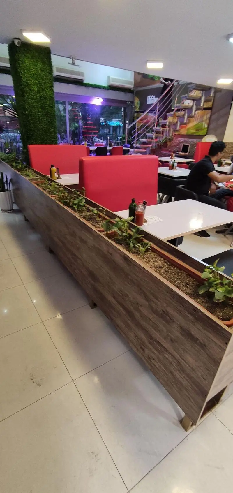 تصویری از فضای داخلی فست فود پدرخوب با دکوراسیون شیک، شامل نیمکت‌های قرمز، میزهای تمیز و دیواره گلدان‌های طبیعی.