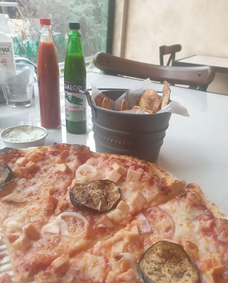 تصویری از پیتزای تازه و داغ پیتزا پای با مرغ، بادمجان و پیاز، سس‌های متنوع تند و ظرف چیپس ترد.