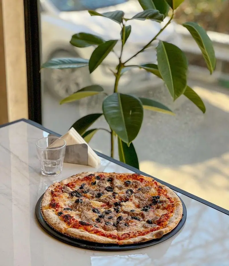 پیتزای گوشت و زیتون سیاه تازه و لذیذ در پیتزا پای، روی میز مرمرین رستوران با محیطی دلنشین. مناسب برای سفارش و سرو در محل.