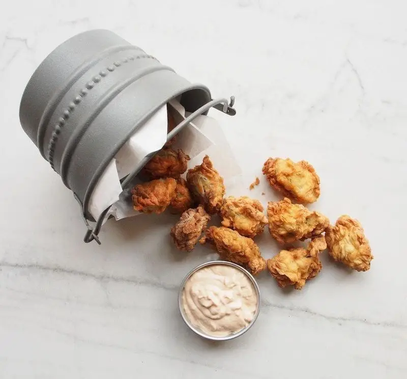 سطل کوچک ناگت‌های مرغ سوخاری طلایی و خوشمزه روی میز مرمر سفید ریخته، با سس دیپینگ کرمی. بهترین کنار پیتزا پای.