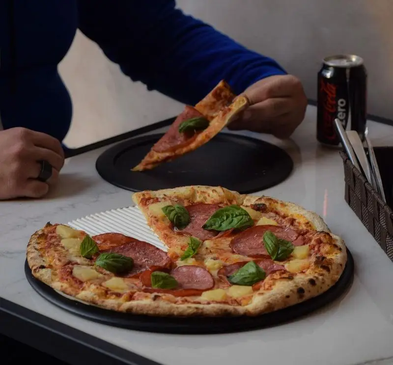 پیتزای پپرونی و آناناس خوشمزه با برگ ریحان تازه در رستوران پیتزا پای، آماده برای سرو و لذت بردن از طعم بی‌نظیر.