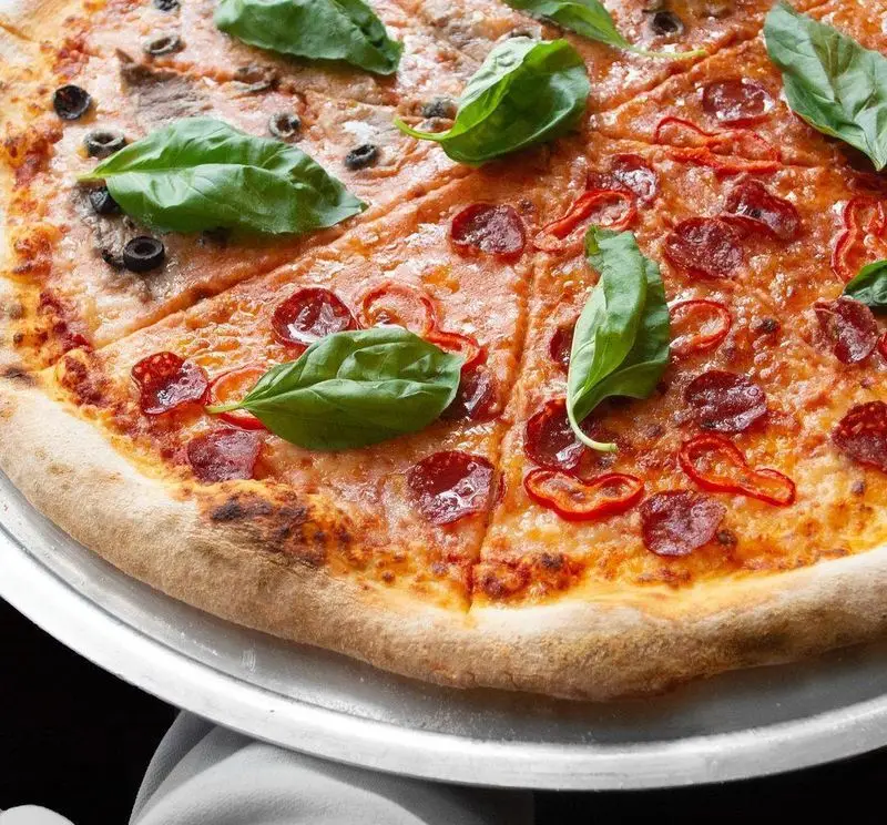 تصویری زیبا از پیتزای دو طعم (پپرونی و زیتون) از پیتزا پای، با پنیر فراوان و ریحان تازه روی نان کریسپی، بهترین انتخاب برای سفارش پیتزا.