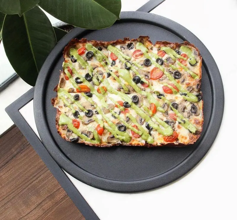 پیتزا مستطیلی خوشمزه کسب و کار پیتزا پای با پنیر، قارچ، زیتون سیاه، گوجه گیلاسی و سس سبز، سرو شده روی سینی مشکی.