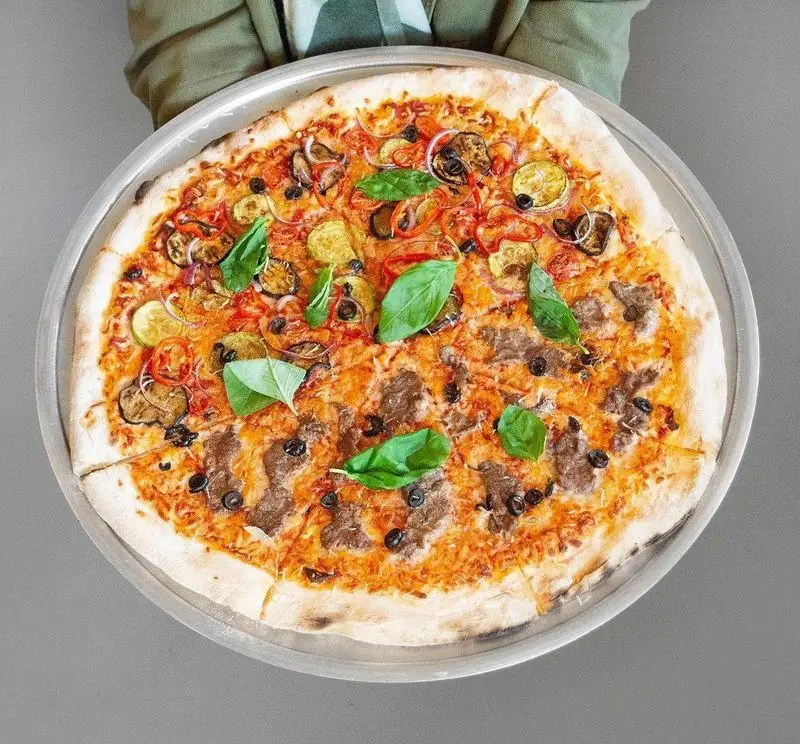 پیتزای بزرگ و خوشمزه پیتزا پای با دو نیمه متفاوت: یک طرف با سبزیجات (بادمجان، کدو، پیاز، فلفل، زیتون) و طرف دیگر با تاپینگ گوشتی و زیتون. روی سینی.