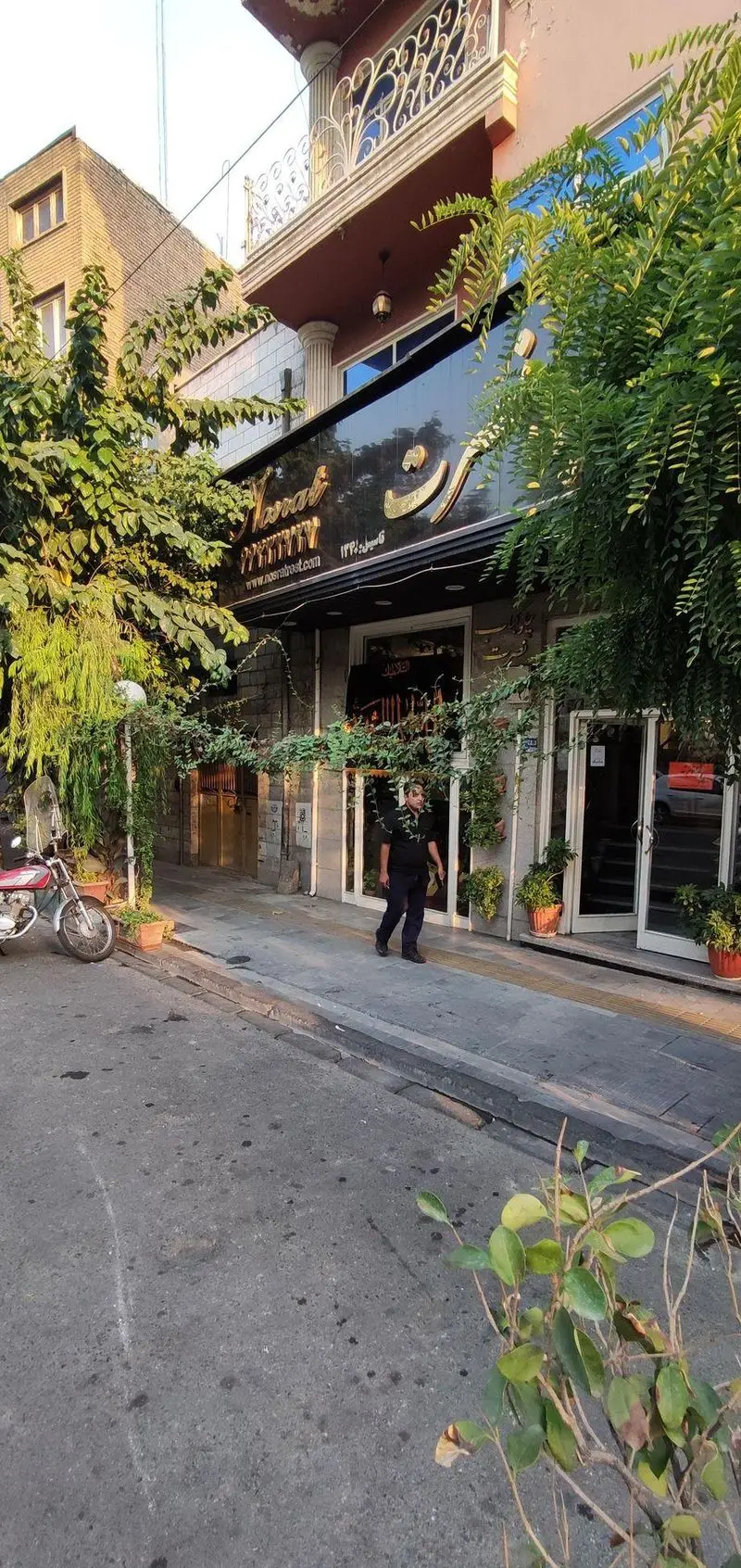 نمای بیرونی چشم‌نواز چلوکبابی نصرت، رستورانی محبوب با تابلوی درخشان، گیاهان سبز و فضای پیاده‌رو. تجربه‌ای اصیل از کباب ایرانی.