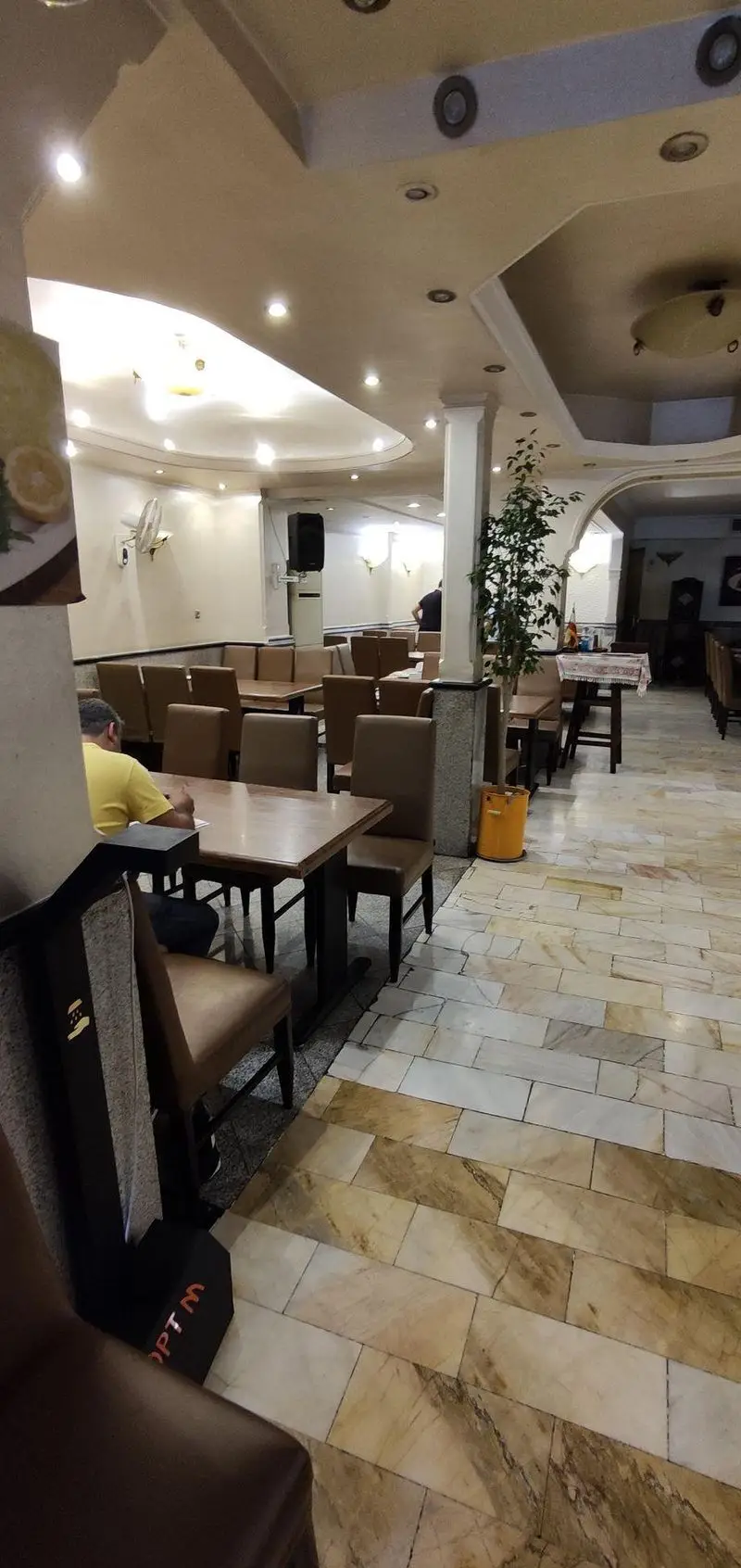 نمای داخلی دنج چلوکبابی نصرت با میز و صندلی‌های چوبی قهوه‌ای، کفپوش مرمر و نورپردازی دلنشین، محیطی عالی برای صرف چلوکباب اصیل.