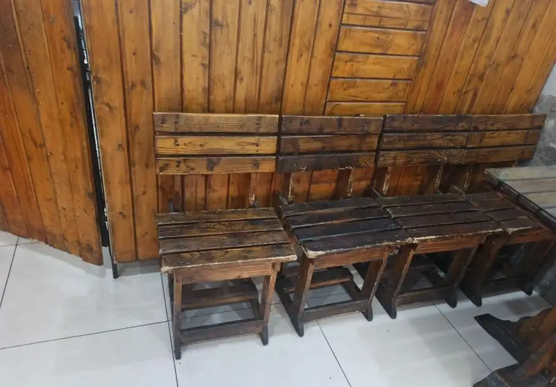 محیط داخلی فست فود مددی: صندلی‌ها و دیوارپوش‌های چوبی با طرح روستیک، فضایی گرم و صمیمی برای مشتریان فراهم آورده است.