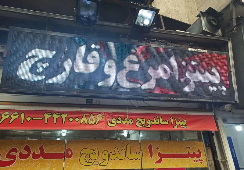 تصویری از نمای شب "فست فود مددی" با تابلو LED "پیتزا مرغ و قارچ" و بنر پیتزا، ساندویچ مددی و تلفن ۶۶۱۰۰-۳۳۲۰۰۸۵۶.