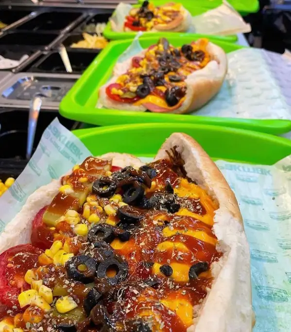 ساندویچ‌های پر ملات و خوشمزه فست فود پک مک با پنیر، ذرت، زیتون و سس‌های متنوع در سینی سبز آماده سرو.