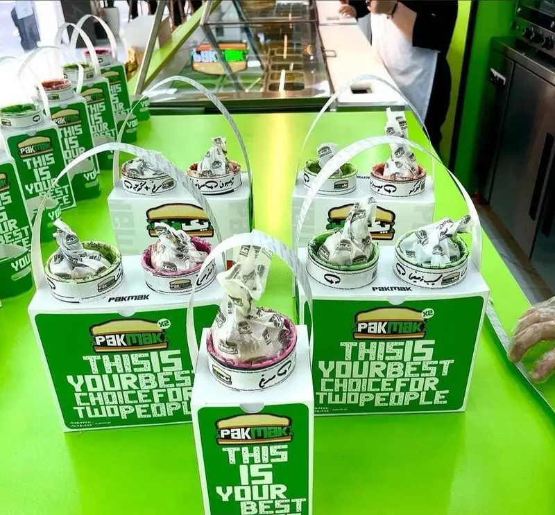 بسته بندی جذاب و جدید فست فود پک مک: جعبه‌های سبز با مینی‌برگرها و ساندویچ‌های متنوع، انتخابی عالی برای یک غذای بیرون‌بر دو نفره.