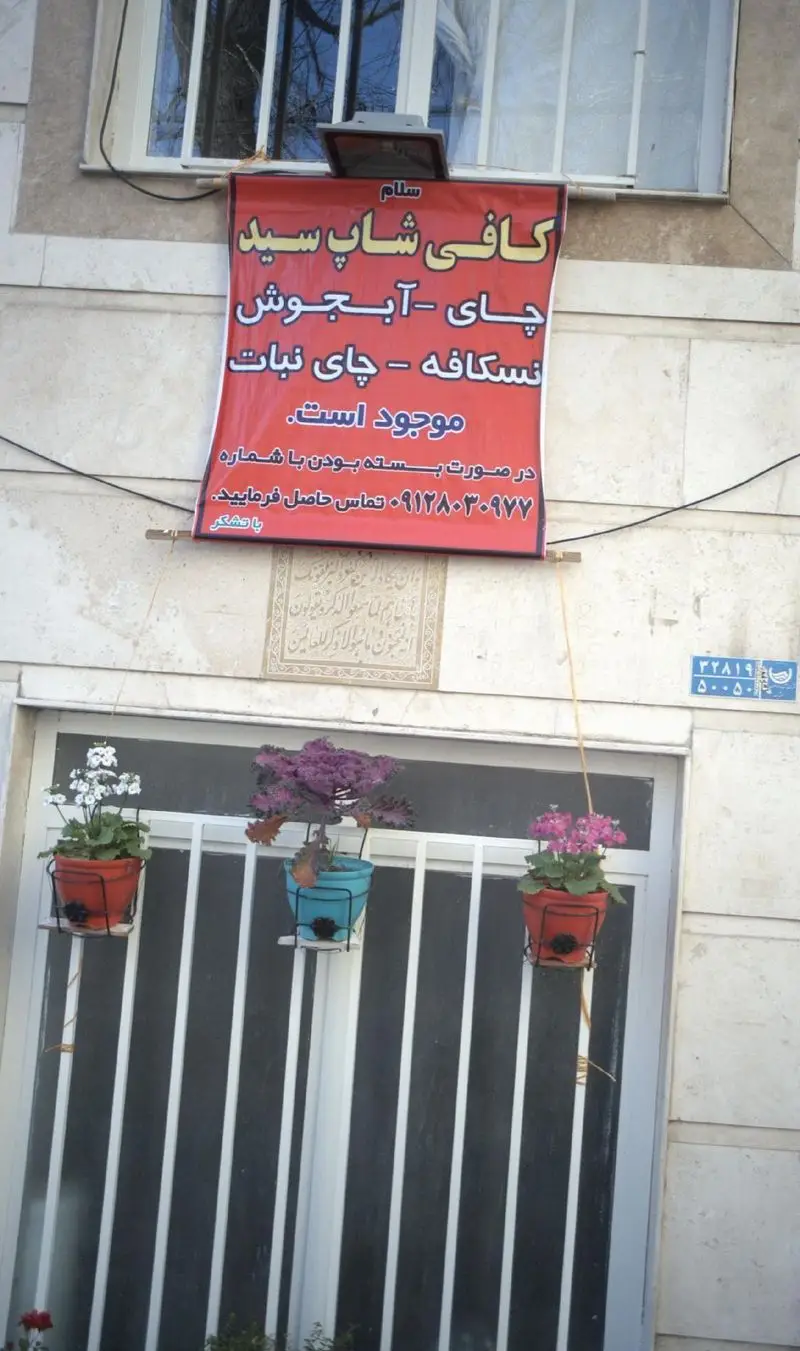 تابلو کافی شاپ سید با لیست محصولات چای، نسکافه، آبجوش، چای نبات و شماره تماس ۰۹۱۲۸۰۳۰۹۷۷ روی دیوار ساختمان.