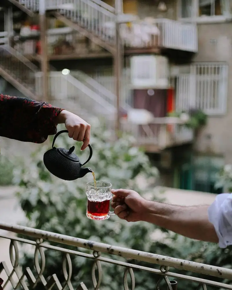 لحظات دلنشین نوشیدن چای تازه و اصیل در کافه ث. سرو چای گرم از قوری چدنی به استکان در فضای باز و دلپذیر کافه.