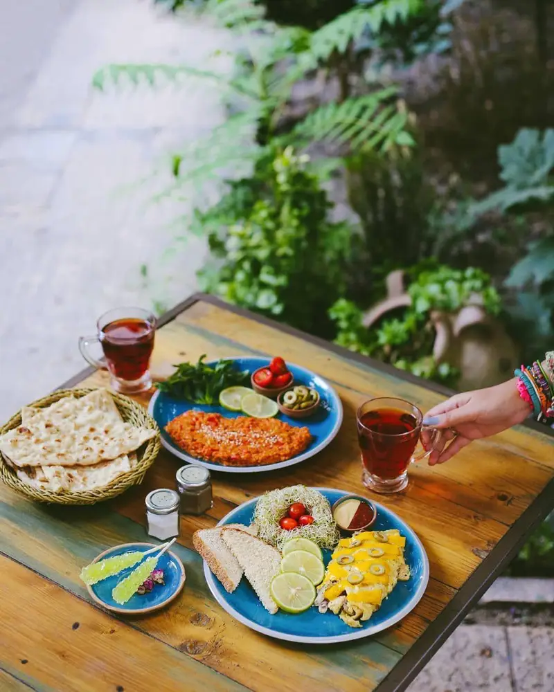 تجربه صبحانه لذیذ در کافه ث: املت سنتی، نان تازه، سبزیجات، زیتون، چای و نبات در فضایی دلنشین و سرسبز.