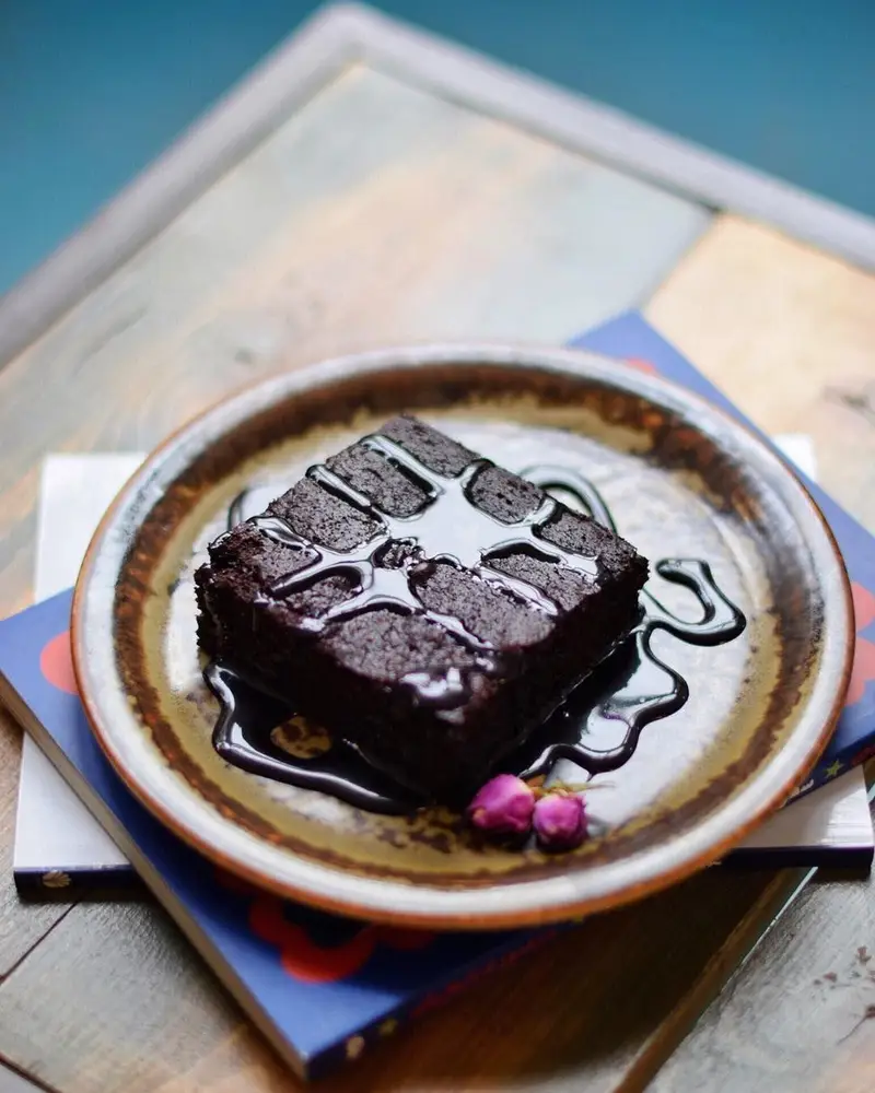 براونی شکلاتی خوشمزه کافه ث با سس شکلات روی یک بشقاب روستیک، دسری دلپذیر برای لحظات شیرین شما.