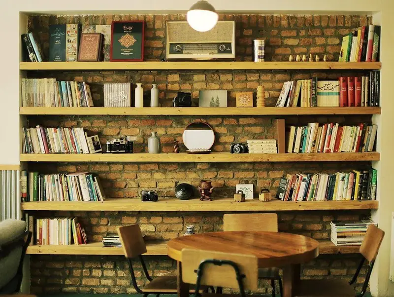 فضای دنج کافه ث با دیوارهای آجری، قفسه‌های چوبی پر از کتاب، رادیو قدیمی و میز چوبی. محیطی آرام برای مطالعه و گفتگو.