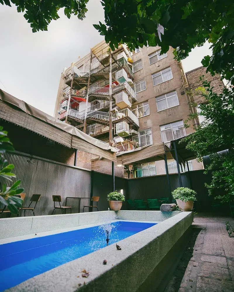 تصویری زیبا از حیاط دلنشین و فضای باز کافه ث، با آبنمای آبی رنگ و محیطی آرامش‌بخش مناسب گفتگو و نوشیدنی‌های فصلی.