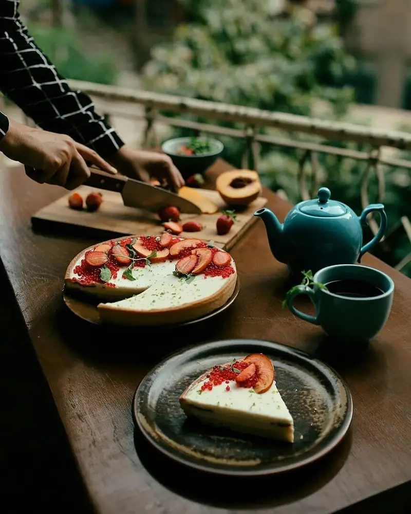 لحظات دلنشین در کافه ث: برش میوه تازه برای تارت توت‌فرنگی و هلو، همراه چای داغ در فضای باز کافیشاپ.
