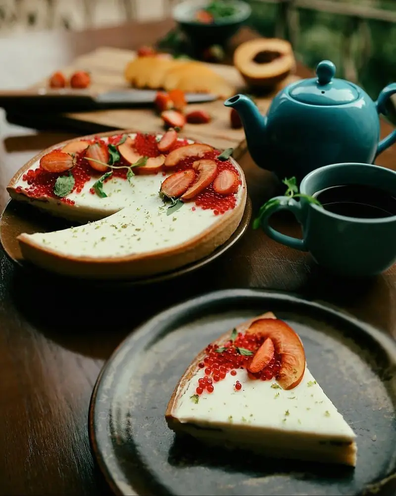 تارت میوه‌ای خوش طعم کافه ث با کرم سفید، توت فرنگی، هلو و مرواریدهای قرمز، سرو شده با چای. یک دسر بی‌نظیر برای تجربه کافه.