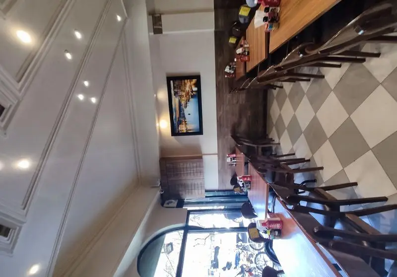 فضای داخلی شیک و دنج فست فود پیتزا میخوش، شامل میز و صندلی‌های چوبی، کف شطرنجی و دیوارهای روشن با تابلوی هنری.