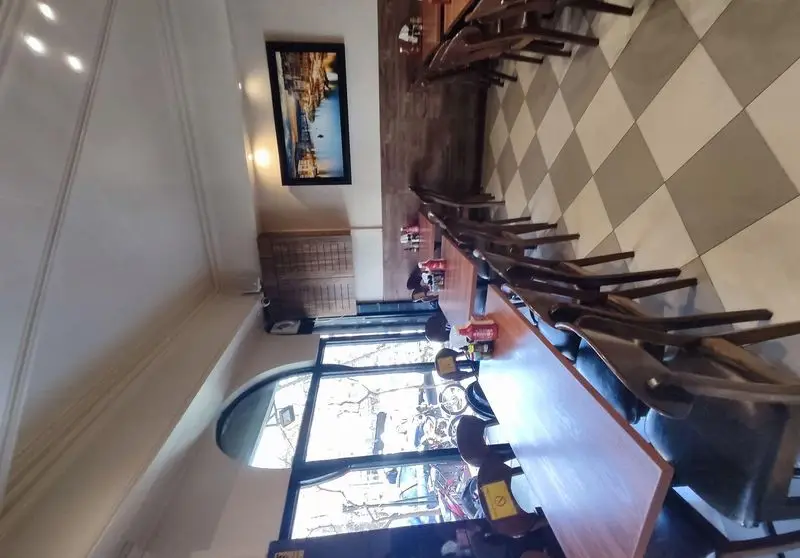 فضای داخلی دنج و چیدمان منظم رستوران فست فود پیتزا میخوش با میز و صندلی‌های چوبی، پنجره بزرگ و کف شطرنجی، آماده پذیرایی از مشتریان.