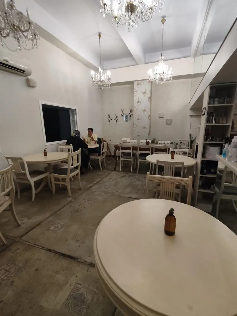 تصویری از فضای داخلی دلنشین و آرام رستوران گیاهی پیور، با میز و صندلی‌های شیک سفید، لوسترهای کریستالی و تزئینات هنری خاص.