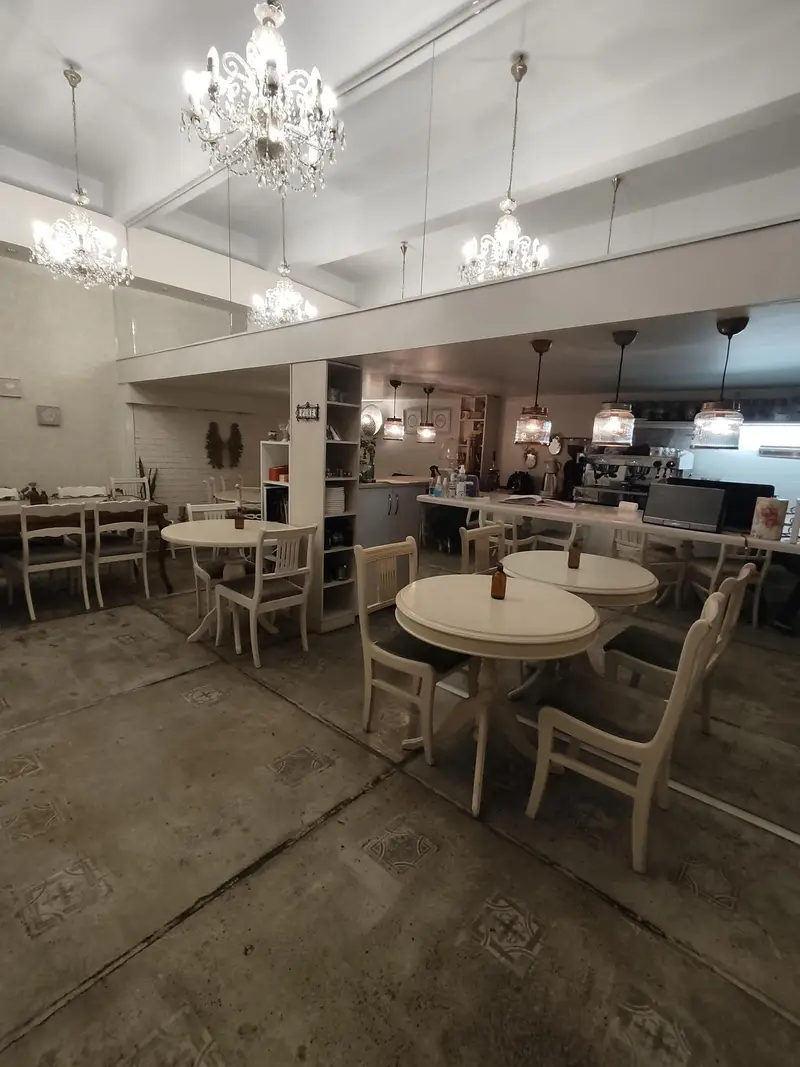 تصویری از دکوراسیون داخلی لوکس رستوران گیاهی پیور. کافه‌ای دنج و شیک با میز و صندلی‌های سفید و لوسترهای کریستالی زیبا.